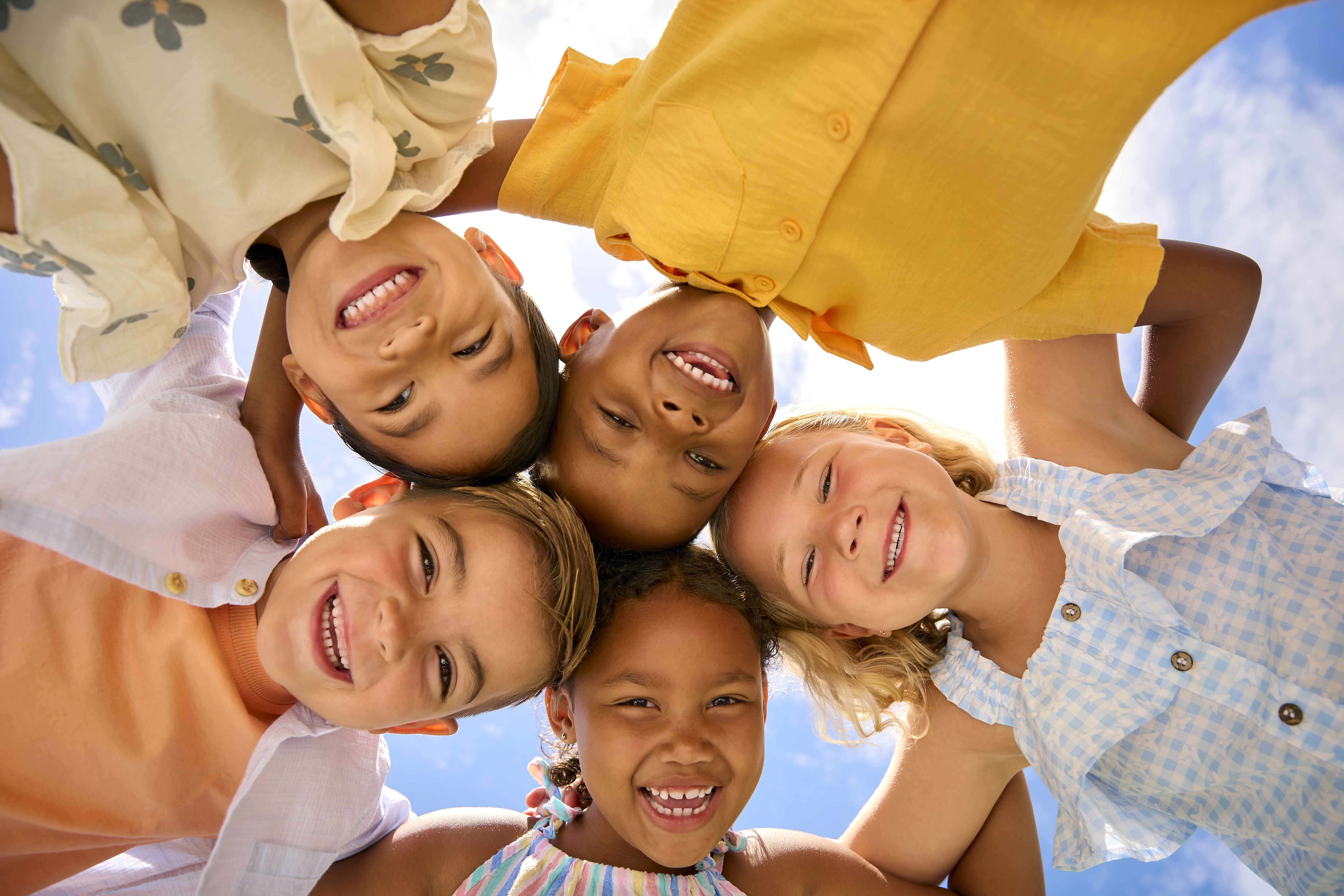 A group of culturally diverse children smiling and hugging in a circle.  